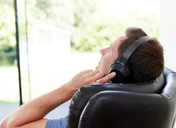 Man Relaxing In Chair At Home Listening To Music Or Podcast Music On Wireless Earphones