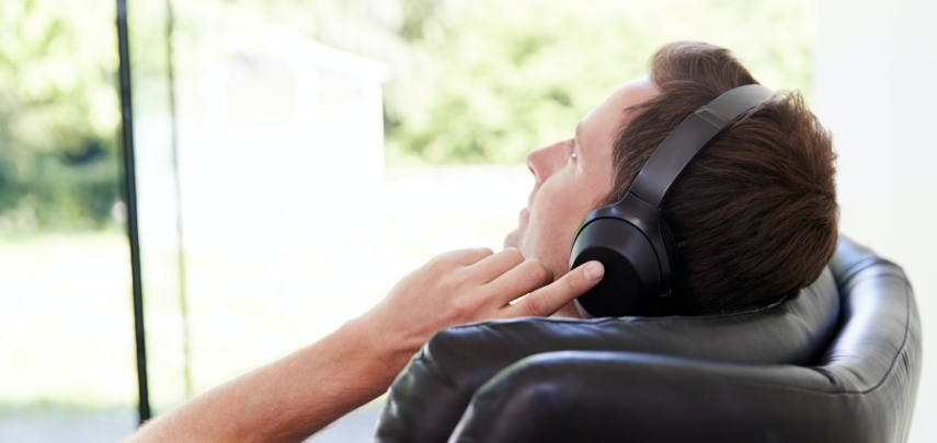 Man Relaxing In Chair At Home Listening To Music Or Podcast Music On Wireless Earphones