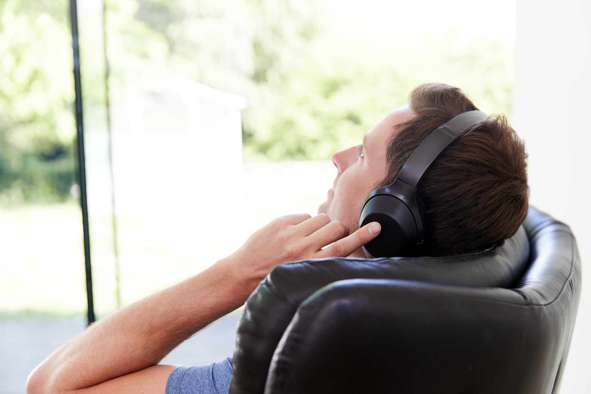 Man Relaxing In Chair At Home Listening To Music Or Podcast Music On Wireless Earphones